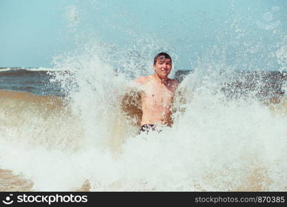 Young man enjoying the high waves in the sea during a summer vacations. Spending a summer holiday by the sea