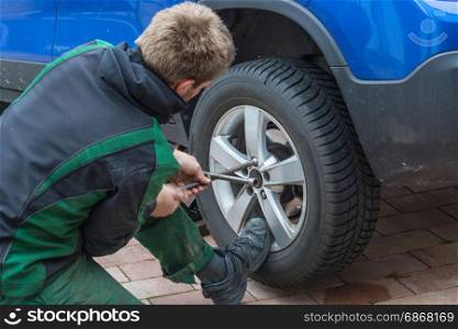 Young man exchanging the car tires. From summer tires on winter tires on his car.