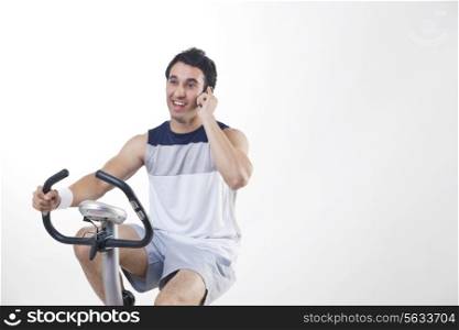 Young man exercising while talking on cell phone over white background