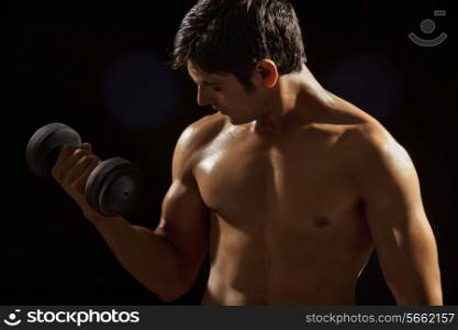 Young man exercising with dumbbell against black background