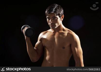 Young man exercising with dumbbell isolated over black background