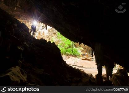 Young man exploring mystery cave with a torch, Phraya Nakhon Cave is a large cave which has a hole in the ceiling allowing sunlight to penetrate, the cave is most popular attraction is a pavilion constructed during the reign of King Rama. Prachuap Khiri Khan, Thailand.