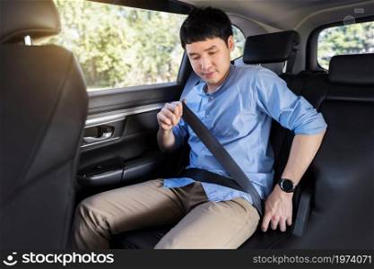 young man fastening a seat belt while sitting in the back seat of car