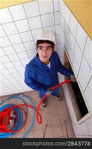 Young man feeding red flexible piping through a large hole in the wall