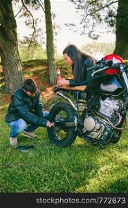 Young man fixing his damaged motorcycle while his girlfriend looks at him taking a beer outdoors. Man fixing his motorcycle while his girlfriend looks at him