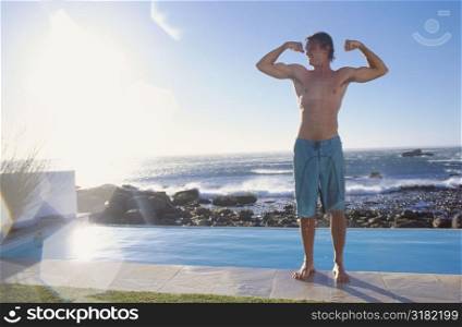 Young man flexing his muscles by the pool