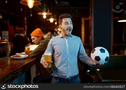 Young man football fun watching sports match at bar and rejoicing. Excited millennial guy holding ball drinking beer for win of favorite soccer team at local pub. Young man football fun watching sports match at bar and rejoicing