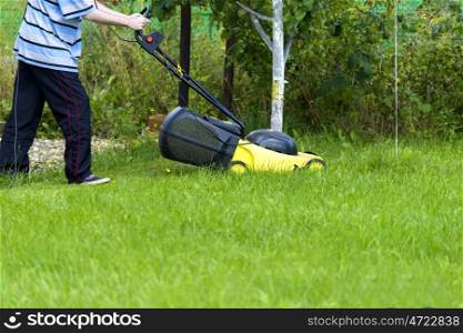 Young man gardener using lawn mower at sunny day