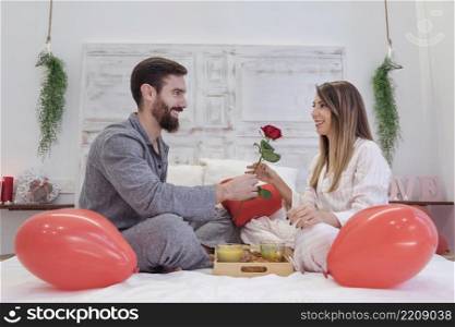 young man giving red rose woman bed