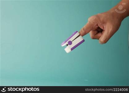 young man hand using pulse oximeter.. close up of man hand using pulse oximeter against light green background 