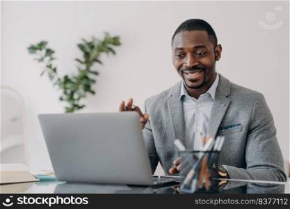 Young man has video conference on laptop. Freelancer is working online at workplace at home and talking to client. Remote african american worker is suit is sitting in front of camera.. Young man has video conference on laptop. Freelancer is working online at workplace at home.