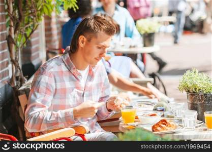 Young man having breakfast at outdoor cafe. Man having breakfastin outdoor restaraunt