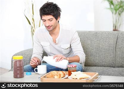 Young man having breakfast in his living room