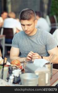 Young man having double cheeseburger in outdoor restaurant