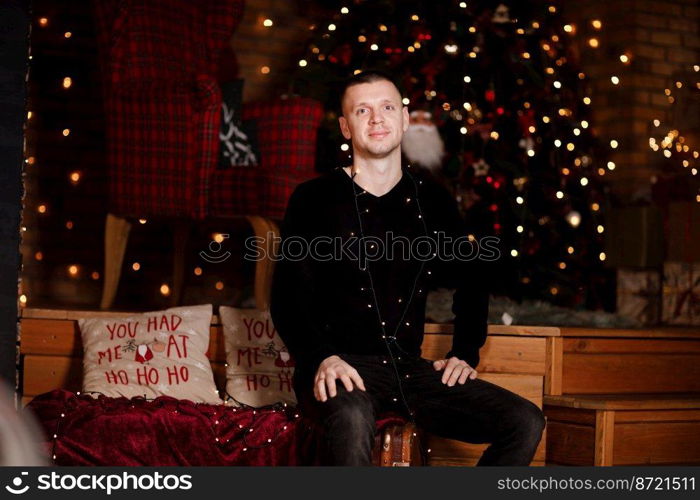 young man having fun near Christmas tree indoors. Portrait of handsome man indoors with Christmas tree and light on background.. young man having fun near Christmas tree indoors. Portrait of handsome man indoors with Christmas tree and light on background