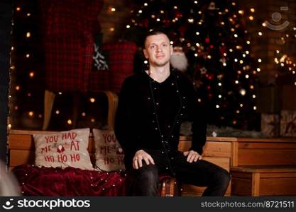 young man having fun near Christmas tree indoors. Portrait of handsome man indoors with Christmas tree and light on background.. young man having fun near Christmas tree indoors. Portrait of handsome man indoors with Christmas tree and light on background