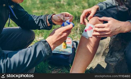 Young man healing knee to a young woman who has been injured doing trekking