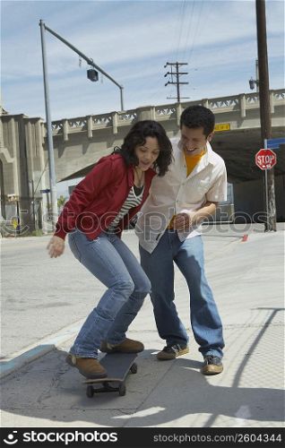 Young man helping a young woman in skateboarding