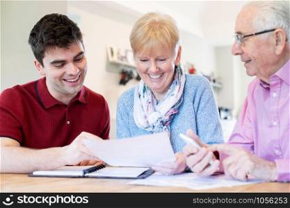 Young Man Helping Senior Couple With Financial Paperwork At Home