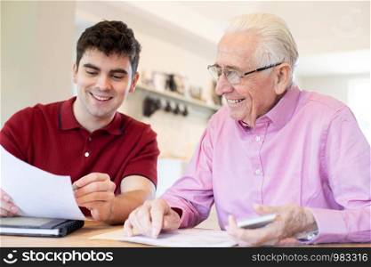 Young Man Helping Senior Neighbor With Paperwork At Home