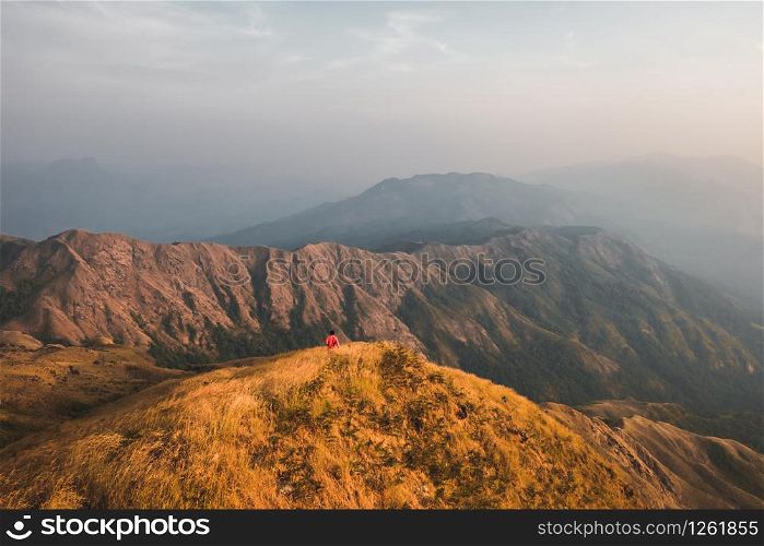 Young man hiking red shirts standing at the middle of a golden meadow mountain view. At Mulayit Taung in Myanmar.