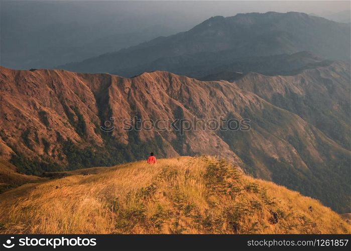 Young man hiking red shirts standing at the middle of a golden meadow mountain view. At Mulayit Taung in Myanmar.
