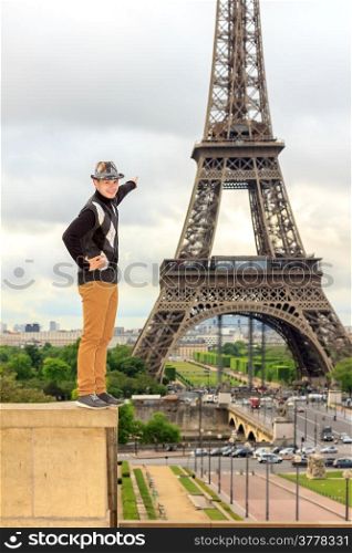 Young man hipster in a hat and vest shows the Eiffel tower (La Tour Eiffel) in Paris, France