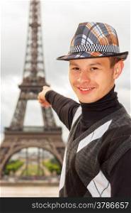 Young man hipster in a hat and vest shows the Eiffel tower (La Tour Eiffel) in Paris, France