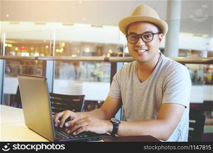 young man hipster working on his laptop in a coffee shop. rear view of business man hands busy using laptop at office desk or young male student typing on computer sitting at wooden table.