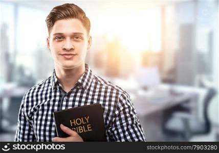 Young man holding a Bible in a modern office (concept for a successful businessman who has principles from the Holy Bible)
