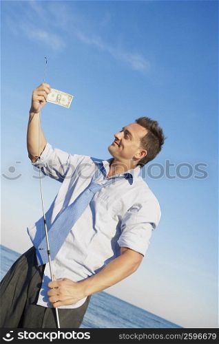 Young man holding a fishing rod and a dollar bill