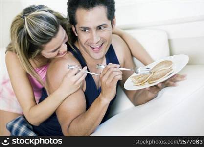 Young man holding a plate of pancakes with a young woman lying on him and smiling
