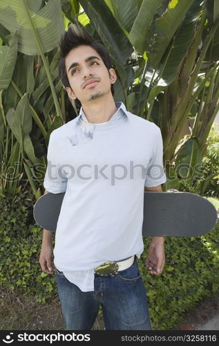 Young man holding a skateboard behind his back