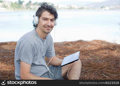 young man holding a tablet with headphones, at the beach