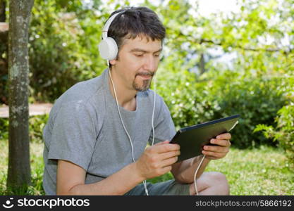 young man holding a tablet with headphones, outdoor