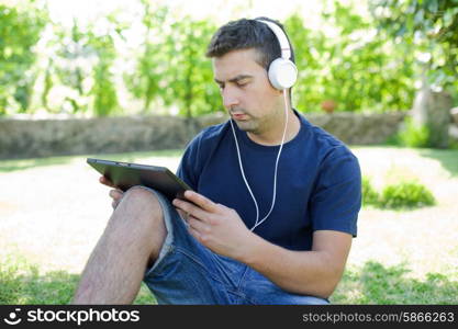 young man holding a tablet with headphones, outdoor