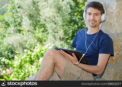 young man holding a tablet with headphones, outdoor