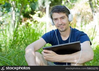 young man holding a tablet with headphones, outdoor