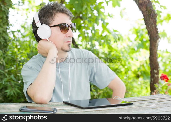 young man holding a tablet with headphones, outdoor