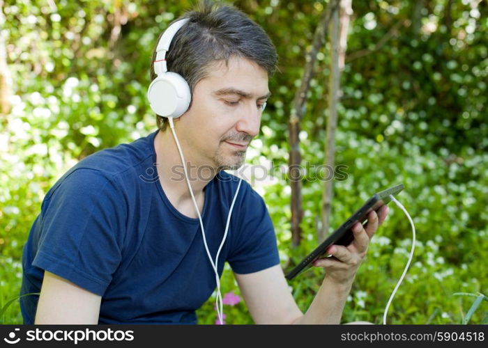 young man holding a tablet with headphones, outdoor