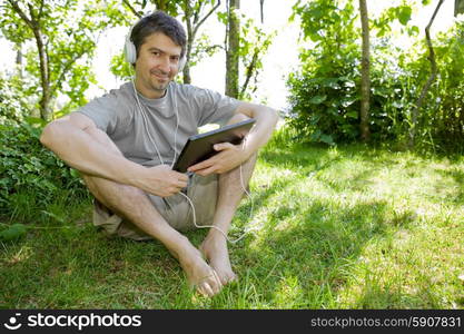 young man holding a tablet with headphones, outdoor