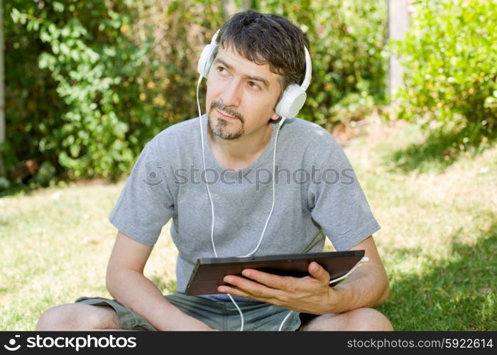 young man holding a tablet with headphones, outdoor