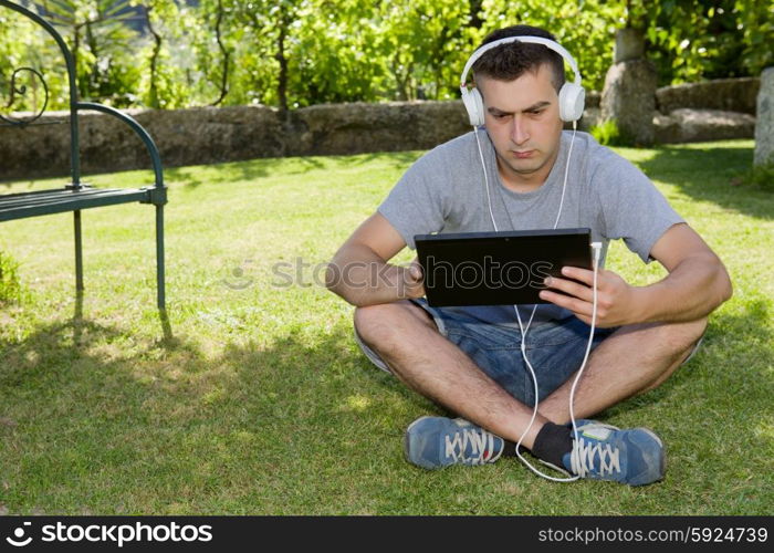 young man holding a tablet with headphones, outdoor