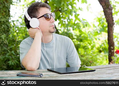 young man holding a tablet with headphones, outdoor