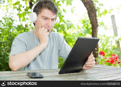 young man holding a tablet with headphones, outdoor