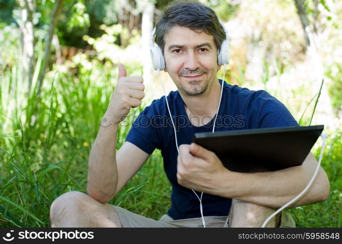 young man holding a tablet with headphones, outdoor