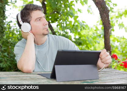 young man holding a tablet with headphones, outdoor