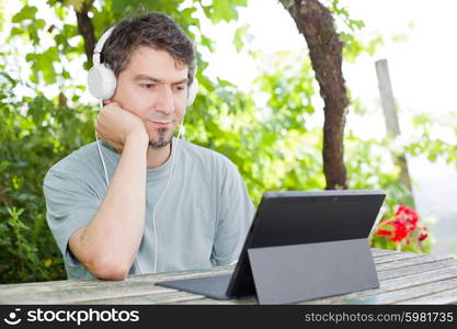 young man holding a tablet with headphones, outdoor