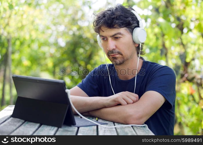 young man holding a tablet with headphones, outdoor