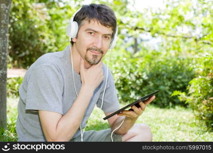 young man holding a tablet with headphones, outdoor